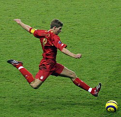 Gerrard wearing an all-red kit and kicking a yellow ball in a match