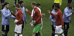 Gerrard, in a red jersey and white shorts, shaking hands with Uruguayan players in 2014