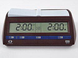 A brown chess clock with blue buttons along the bottom. A digital display shows the time remaining for each side